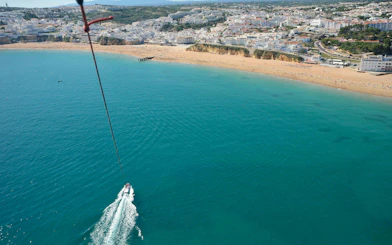 Parasailing over Albufeira coastline with boat below.