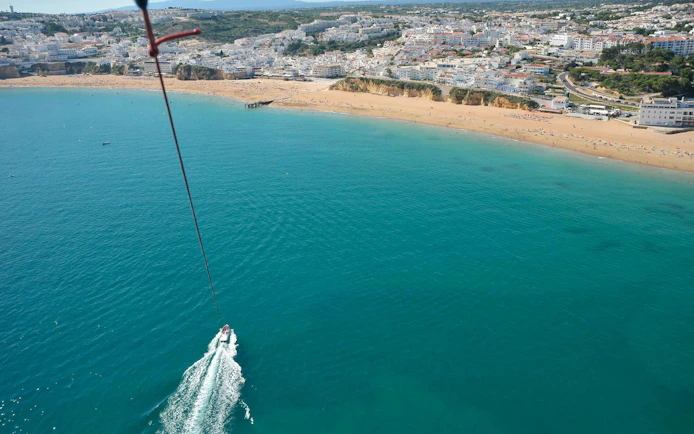Parasailing over Albufeira coastline with boat below.