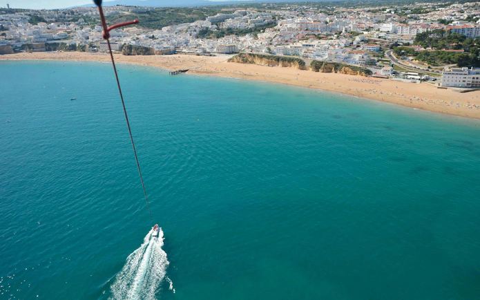Parasailing over Albufeira coastline with boat below.