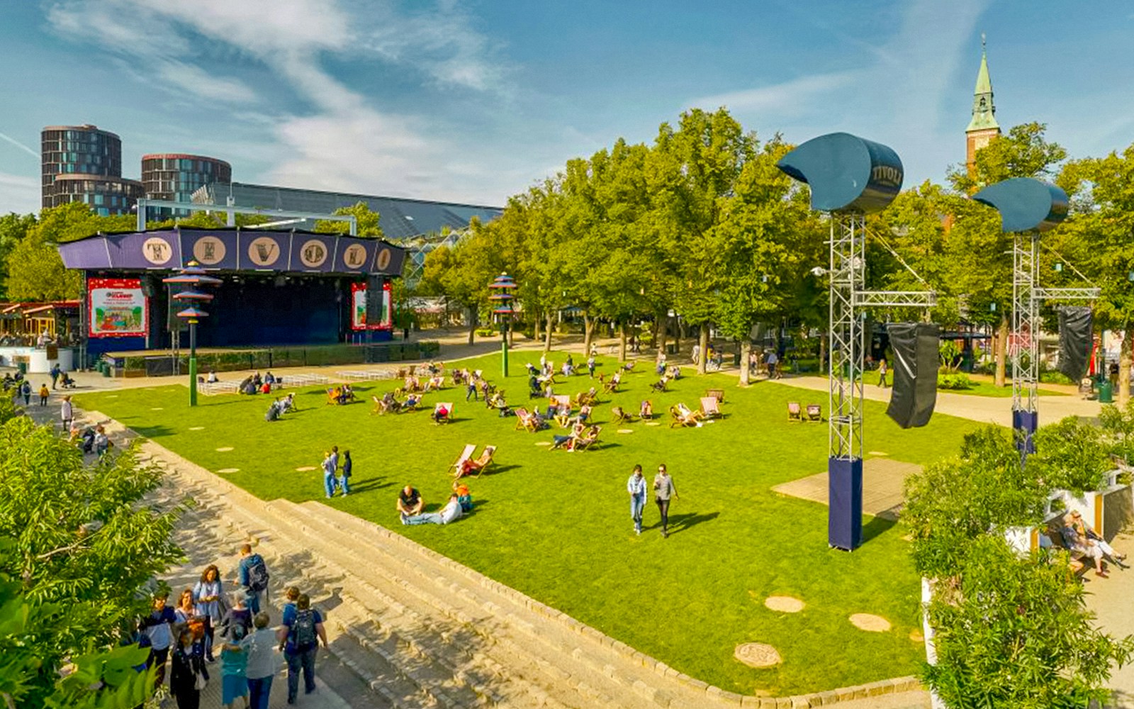 Tivoli Gardens lawn with people relaxing, stage and trees in Copenhagen.
