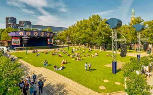 Tivoli Gardens lawn with people relaxing, stage and trees in Copenhagen.