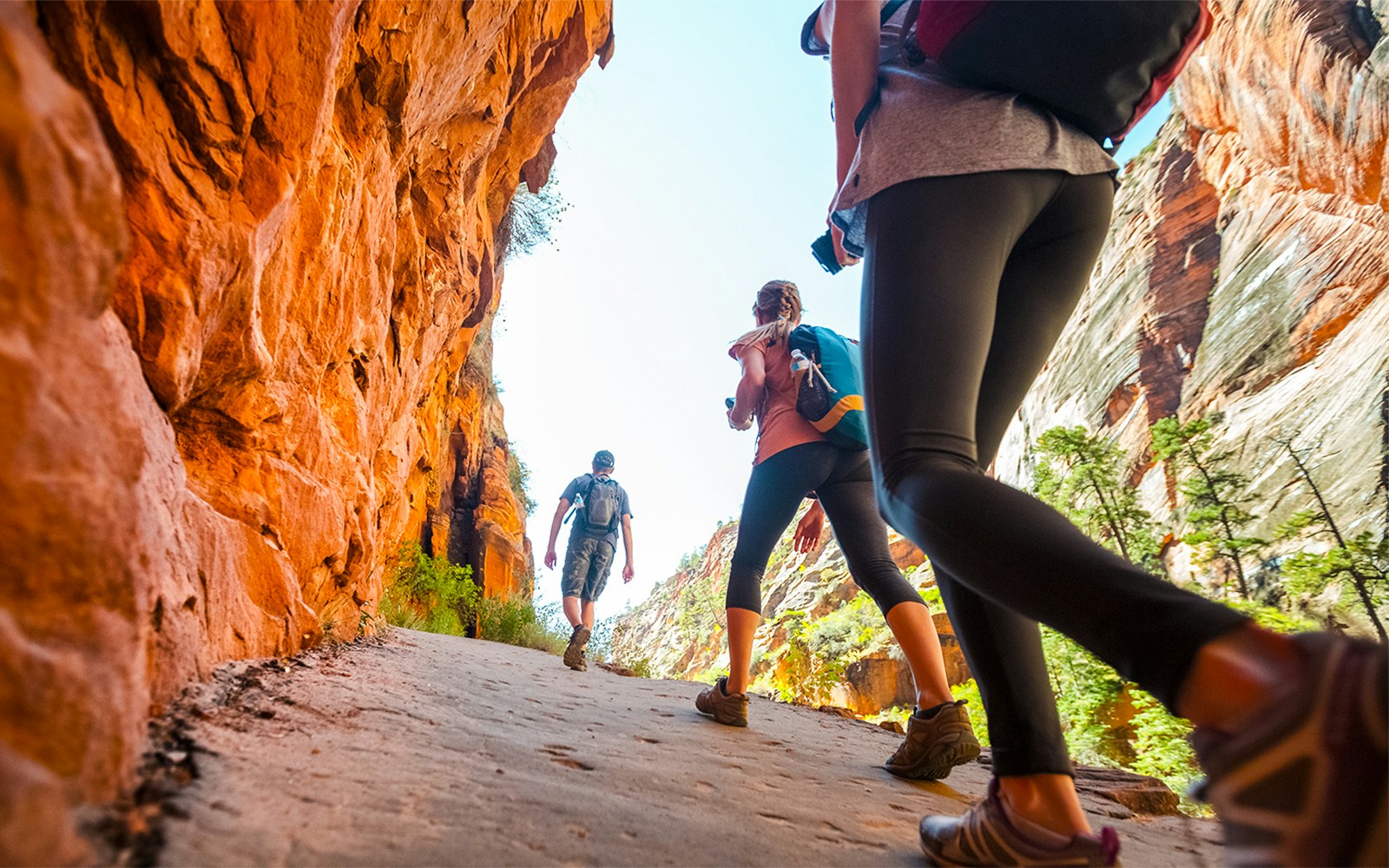 Hikers walking through a narrow canyon with red rock walls.