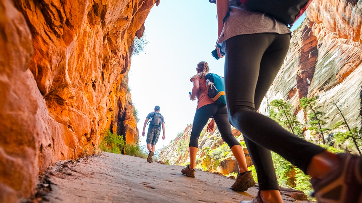 Hikers walking through a narrow canyon with red rock walls.