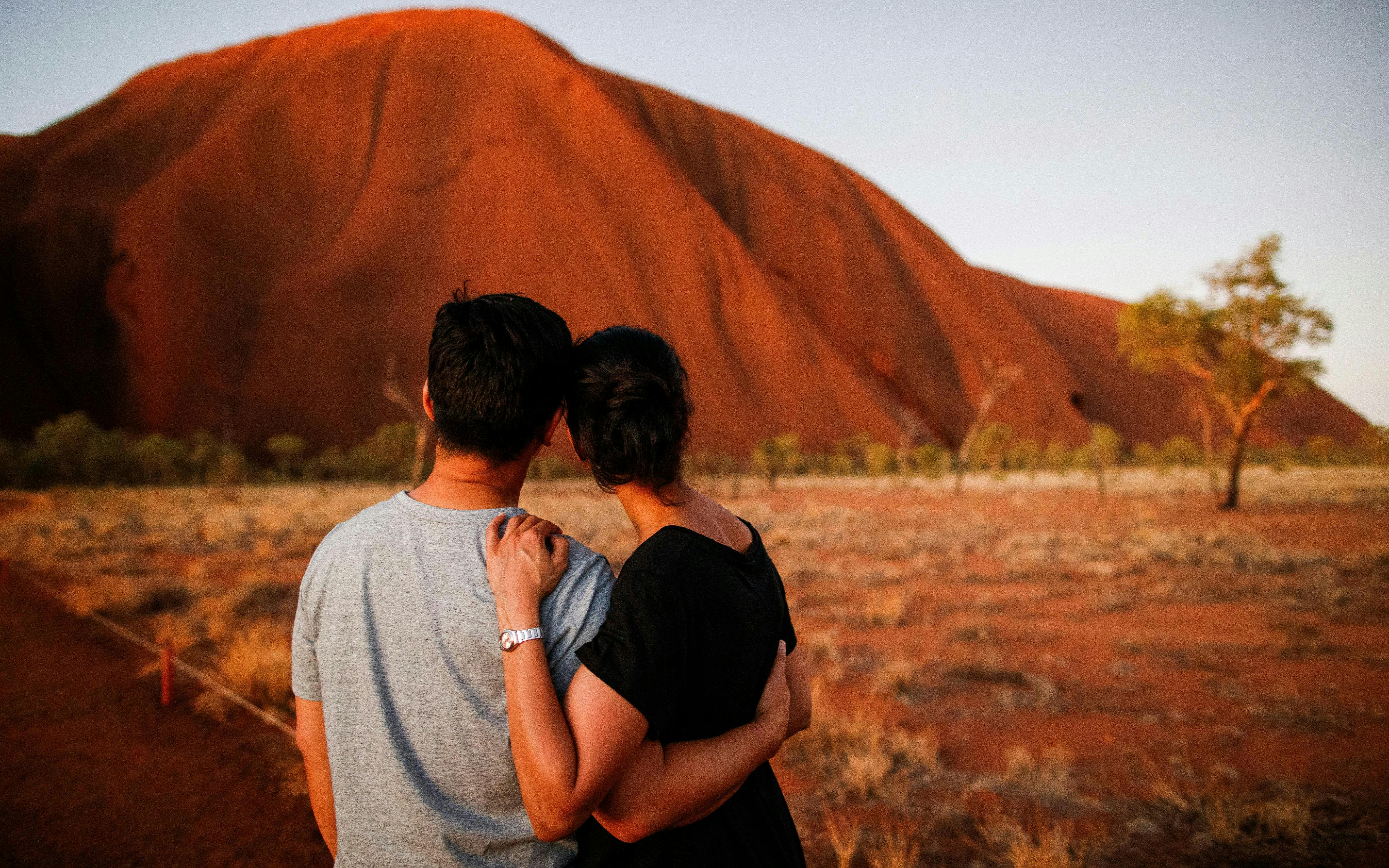 Couple admiring sunrise at Uluru during Kata Tjuta tour, Australia.