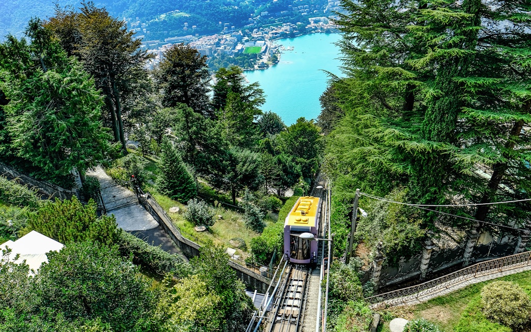 Funicular railway ascending through trees with Lake Como in the background, Italy.