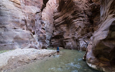 Hiker walking through Wadi Mujib Canyon's narrow water path, Jordan.