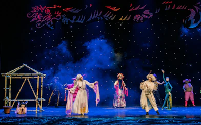 Theatrical performance of The Dragon Child in Sydney with colorful costumes and bamboo structure.