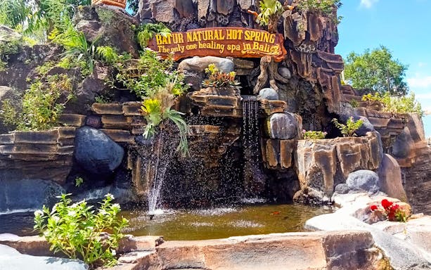 Batur Natural Hot Spring entrance with cascading water and lush greenery in Bali.