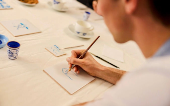 Guest painting a Dutch blue tile at a workshop table.