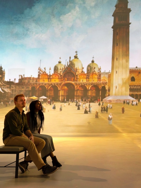 Tourists viewing a gallery exhibit featuring a historical cityscape.
