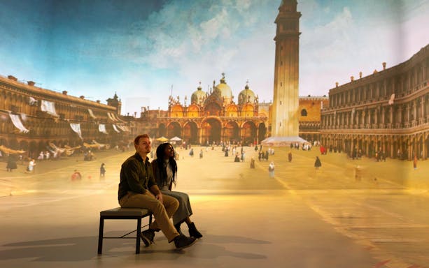 Tourists viewing a gallery exhibit featuring a historical cityscape.