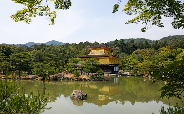 Kinkaku-ji Temple in Kyoto, Japan, reflected in a tranquil pond surrounded by lush greenery.