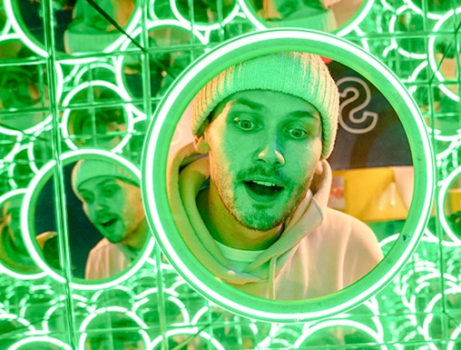 Man in a beanie surrounded by green neon mirrors at World of Illusions, Dublin.