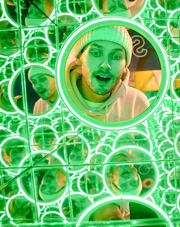 Man in a beanie surrounded by green neon mirrors at World of Illusions, Dublin.