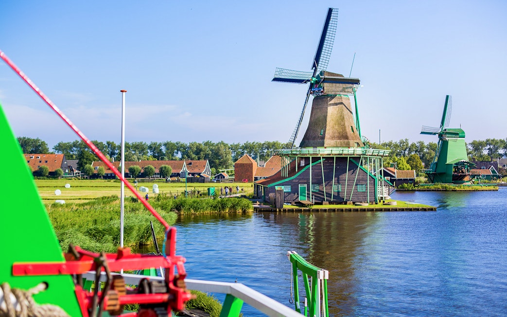 Windmills at Zaanse Schans by the water with traditional Dutch houses in the background.