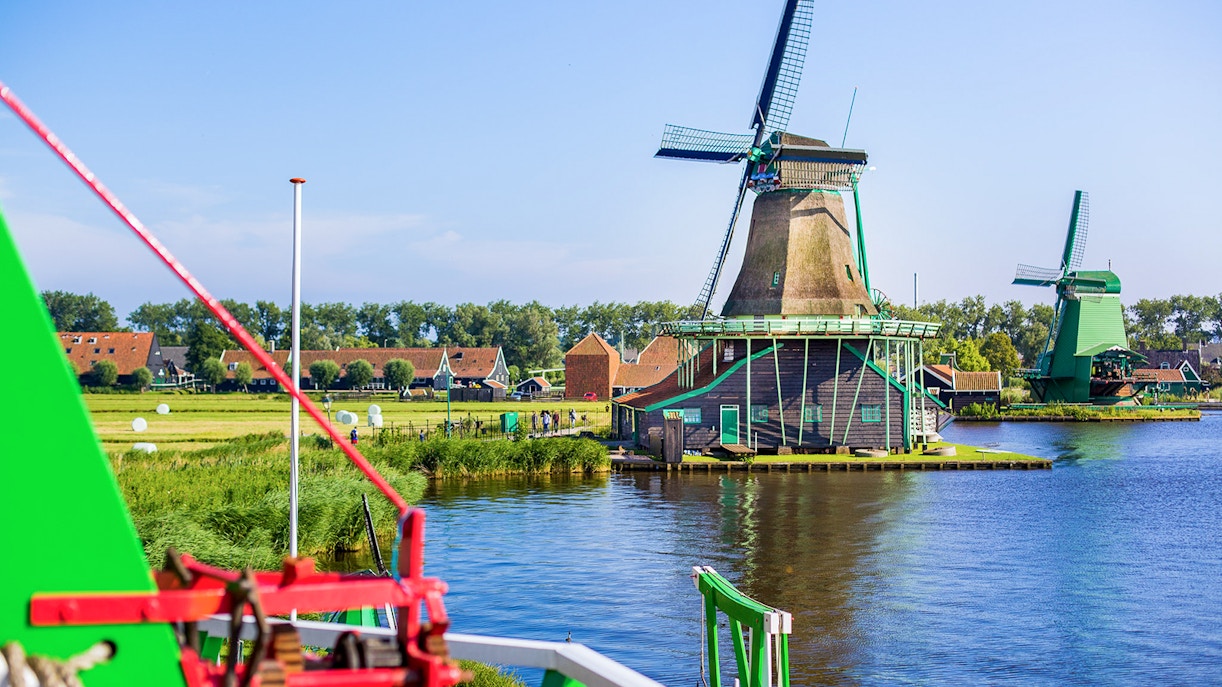 Windmills at Zaanse Schans by the water with traditional Dutch houses in the background.