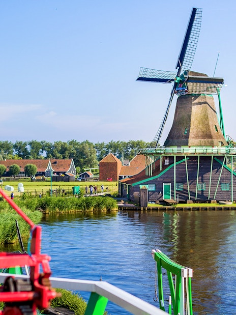Windmills at Zaanse Schans by the water with traditional Dutch houses in the background.