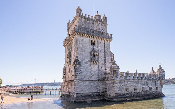 Belém Tower in Lisbon with tourists on a nearby walkway.