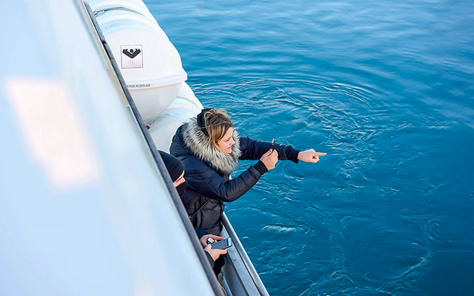 Guests pointing at whales from yacht during whale watching tour.