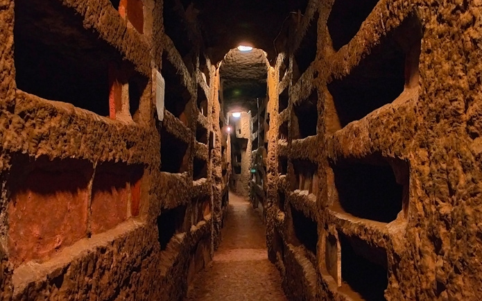 Catacombs of Saint Agnes in Rome with ancient burial niches along a narrow passage.
