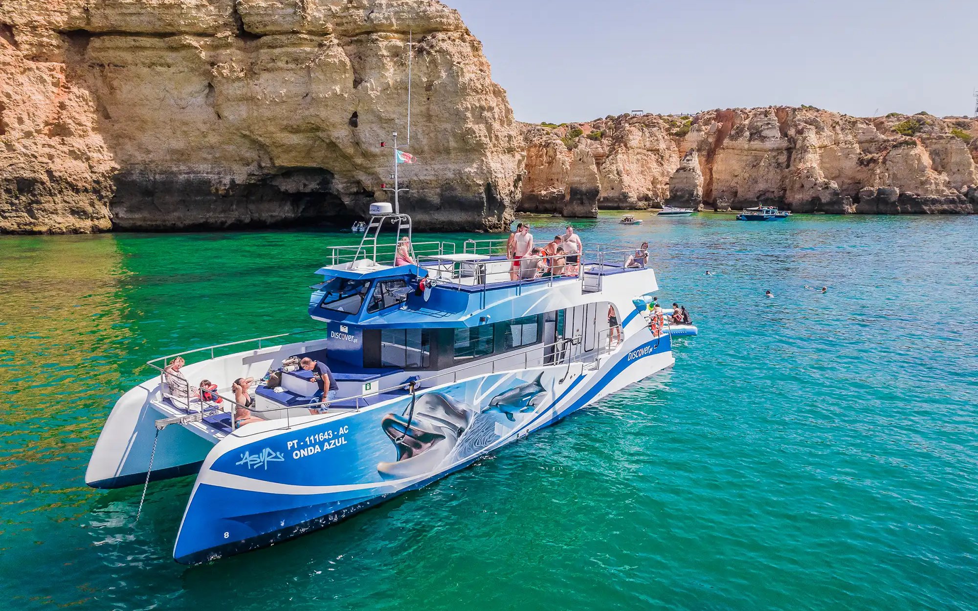 Tourists on a catamaran near Benagil Caves during a dolphin watching tour in Algarve, Portugal.