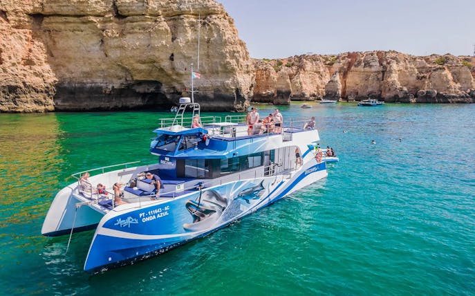 Tourists on a catamaran near Benagil Caves during a dolphin watching tour in Algarve, Portugal.