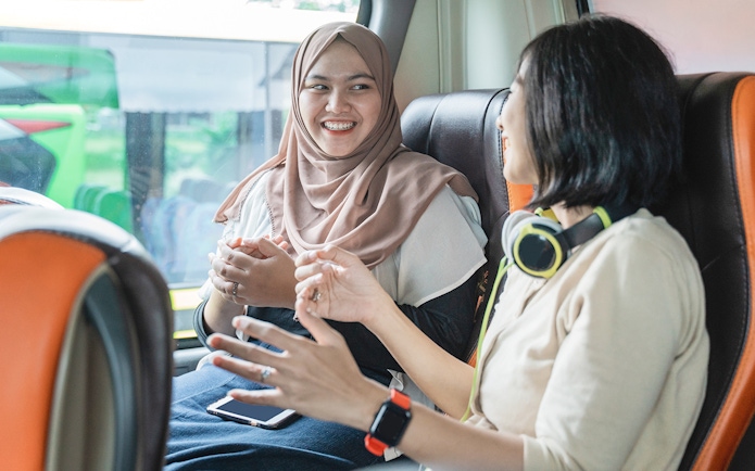 Women chatting on a bus, one wearing headphones, enjoying a conversation.