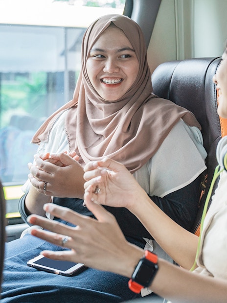 Women chatting on a bus, one wearing headphones, enjoying a conversation.