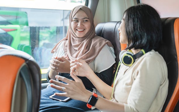 Women chatting on a bus, one wearing headphones, enjoying a conversation.
