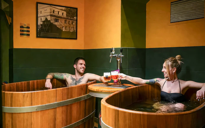 Couple enjoying beer spa in wooden tubs at Budapest's Lukács Thermal Bath.