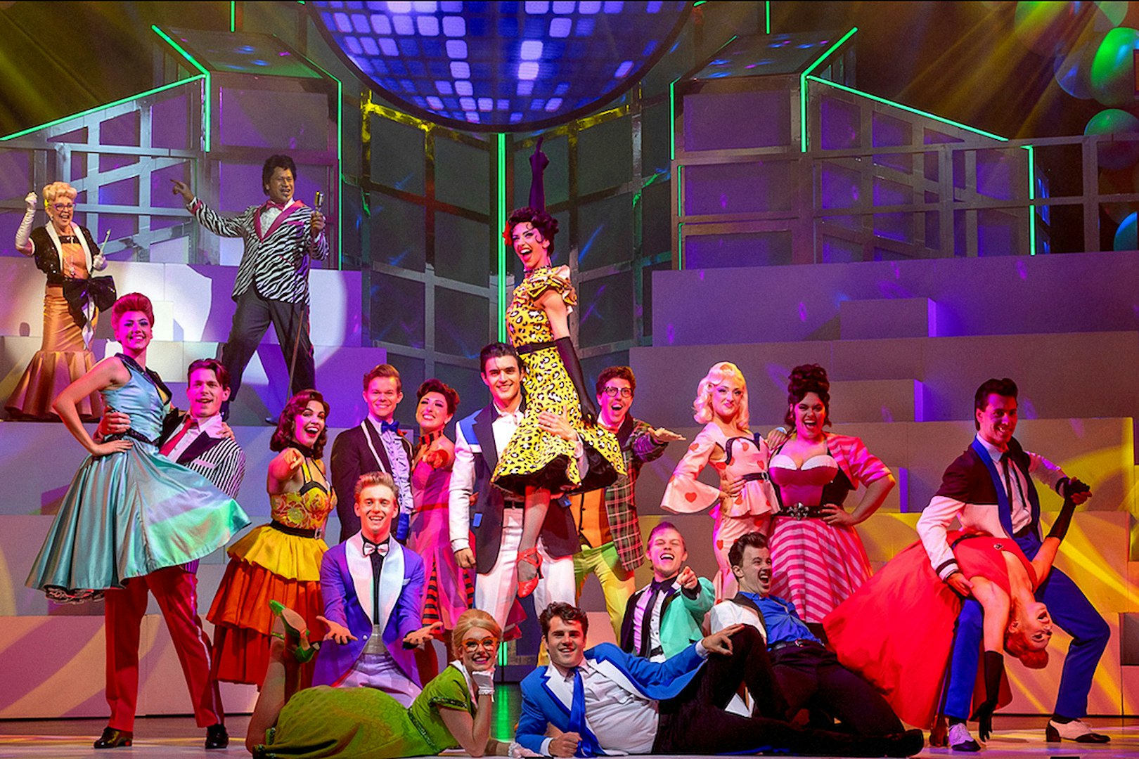 Musical cast performing a lively dance scene from Grease on stage.