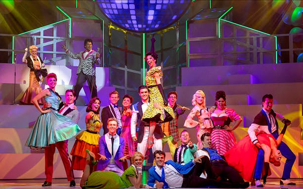 Musical cast performing a lively dance scene from Grease on stage.