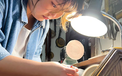 Person crafting amber jewelry under a lamp at Gdańsk Amber Workshop.
