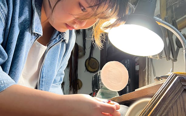Person crafting amber jewelry under a lamp at Gdańsk Amber Workshop.