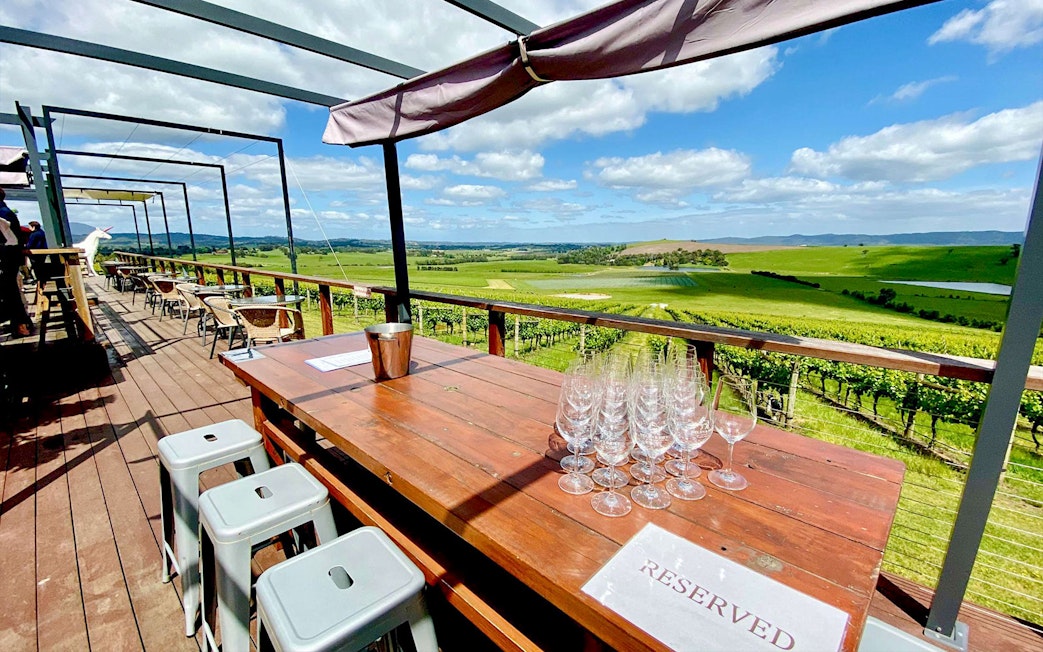 Outdoor seating with wine glasses overlooking Yarra Valley vineyards on a sunny day.