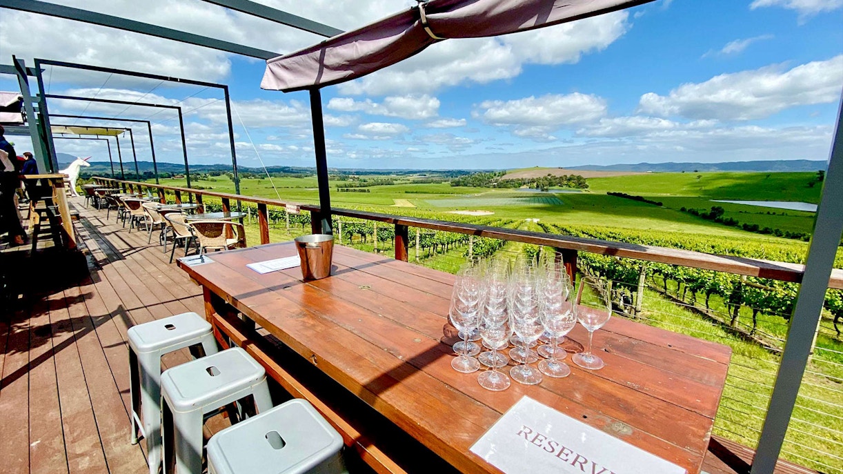 Outdoor seating with wine glasses overlooking Yarra Valley vineyards on a sunny day.