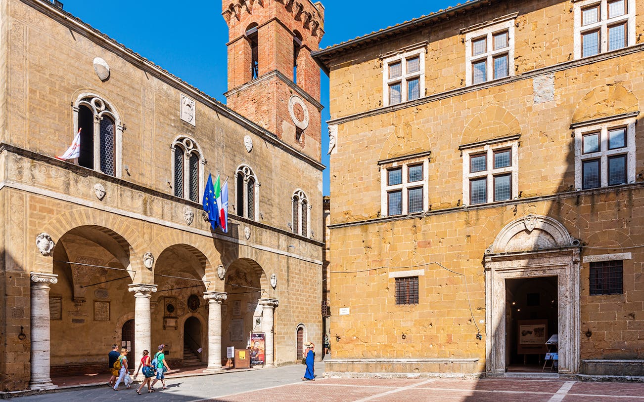 Central Museum and Palazzo Piccolomini in Pienza, Italy, with visitors walking nearby.