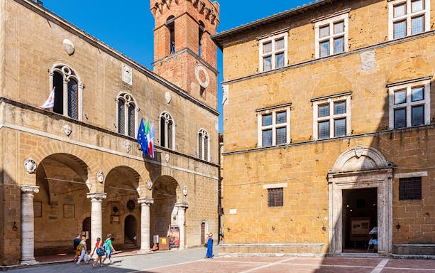 Central Museum and Palazzo Piccolomini in Pienza, Italy, with visitors walking nearby.