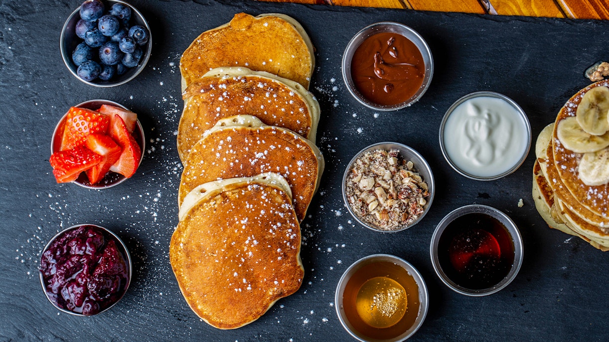 Vier niederländische Pfannkuchen auf einem Teller mit Heidelbeeren, Erdbeeren und Trockenfrüchten und verschiedenen Beilagen, wie Marmelade und Nutella