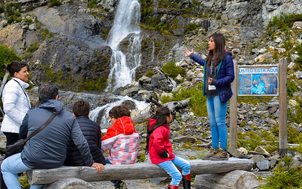 Guide explaining Mayo Spirit Trek to tourists near waterfall in Los Glaciares National Park, Patagonia.