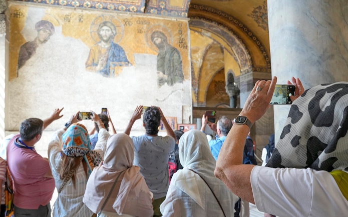 Tourists photographing mosaics inside Hagia Sophia with a guide.