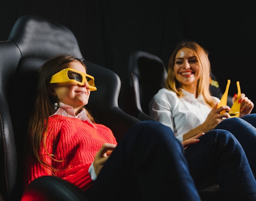 Mother and daughter enjoying 3D movie with glasses in cinema.