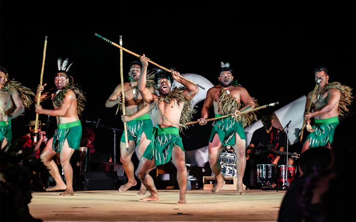 Performers with traditional attire and sticks on stage at Mauka Warriors Luau cultural night show.
