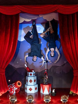 Upside Down Berlin Museum exhibit with performers on ceiling, circus props, and red curtains.