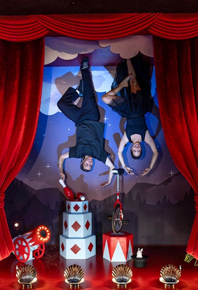 Upside Down Berlin Museum exhibit with performers on ceiling, circus props, and red curtains.