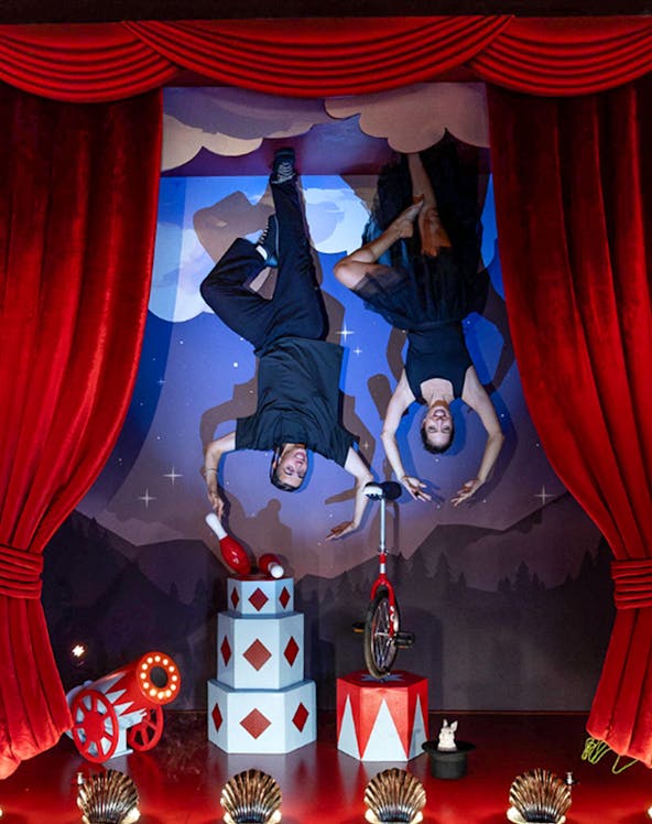 Upside Down Berlin Museum exhibit with performers on ceiling, circus props, and red curtains.