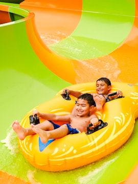 Children enjoying a water slide on a yellow raft at Hurricane Harbor, Six Flags Arlington.