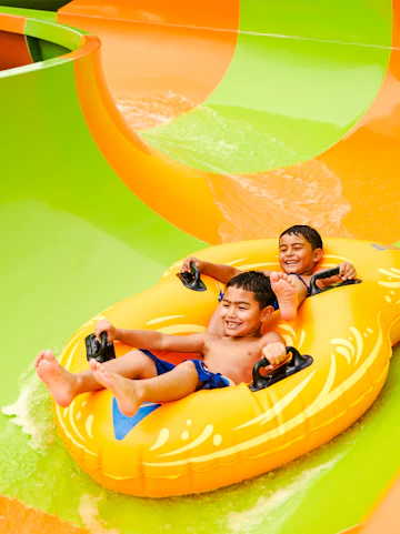 Children enjoying a water slide on a yellow raft at Hurricane Harbor, Six Flags Arlington.