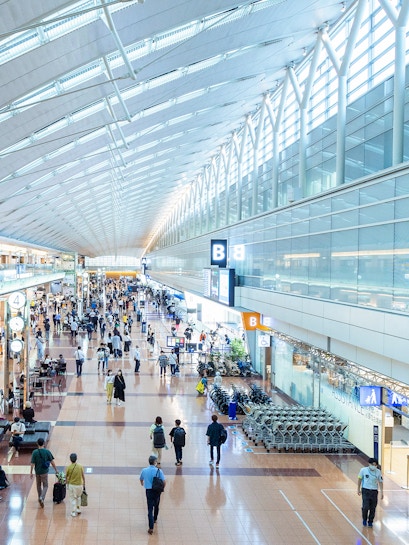 Haneda Airport terminal with travelers walking through concourse, Tokyo, Japan.