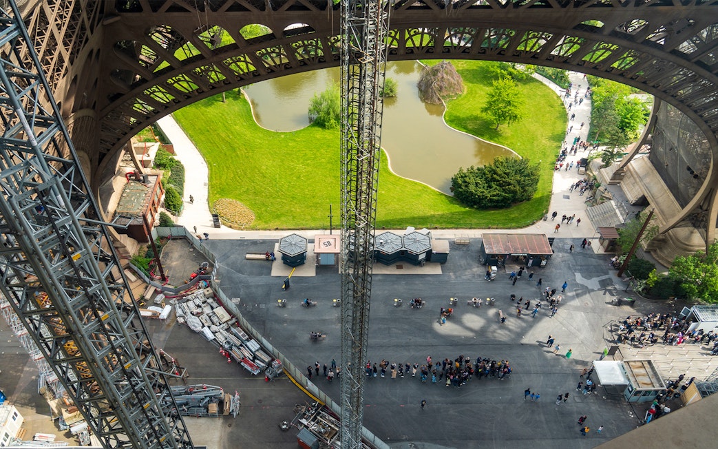 Eiffel Tower view from elevator, showing base structure and surrounding park in Paris.